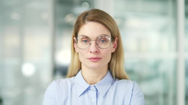 Close up portrait of a confident mature businesswoman in a modern office. Head shot of a serious stylish blonde female employee in glasses is looking at the camera. A successful manager or lawyer