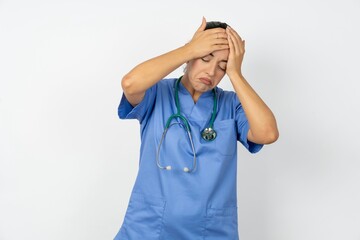 Beautiful doctor woman standing over white studio background suffering from strong headache desperate and stressed because of overwork. Depression and pain concept.