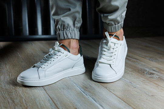 Casual white sneakers for men. Male legs in white leather summer shoes. Comfortable men's white sneakers with laces.