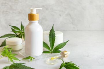 White One pump bottle near green cannabis leaves on white table. Cosmetic Mockup