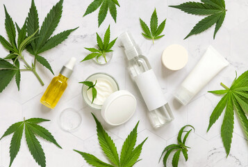 Cosmetic bottles, jars and tubes with blank label near green cannabis leaves. Mockup