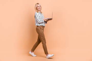 Fototapeta na wymiar Full length profile photo of cheerful nice person use netbook walking isolated on beige color background