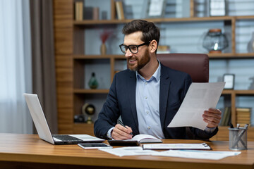 Obraz premium Mature businessman in shirt doing paperwork, man working with documents, contracts and bills sitting at table using laptop at work, financier accountant with beard and glasses