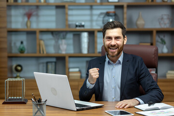 Fototapeta na wymiar Portrait of mature senior businessman in office, man looking at camera and holding hands up super power and superhero gesture, successful investor using laptop inside building.