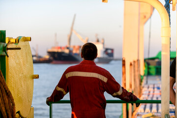 Seaman in red working overall and orange helmet on deck. Working at sea. Cargo vessel. Mooring...