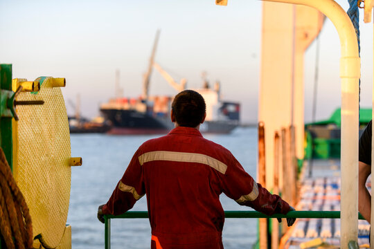 Seaman in red working overall and orange helmet on deck. Working at sea. Cargo vessel. Mooring operations. Able seaman.