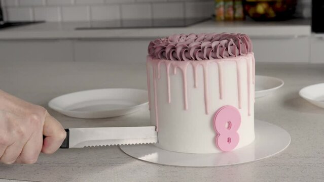 Hand cuts cake with number 8 with knife. Children's birthday with pink cake. Holiday and fun with a feast