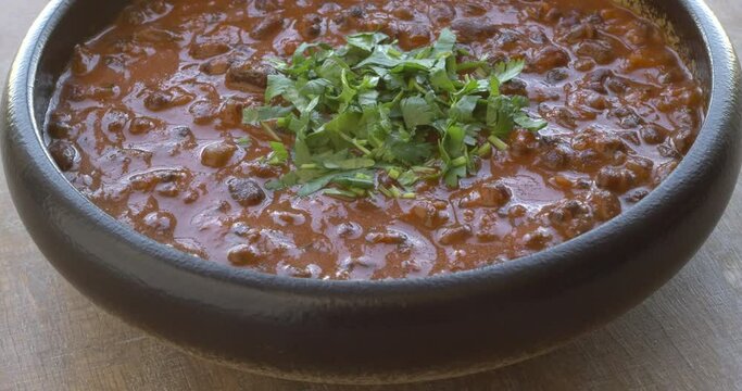 Dal Makhani Punjabi dish made of whole black lentil and adzuki bean, topped with chopped coriander. Table spin.