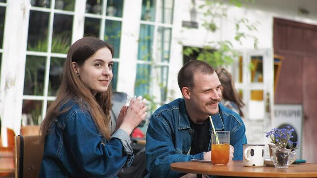 A young couple. Denim clothes. On a date in a vintage restaurant, outside. They are talking. Fooling around