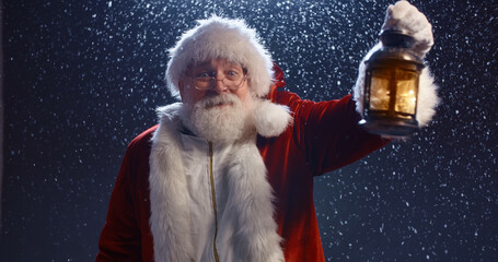 Santa clause holding lantern, searching for something, looking at camera, isolated on snowy blue...