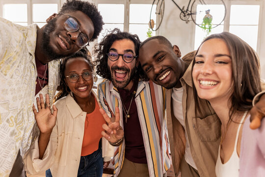 group of cheerful mutliracial coworkers taking selfie using smartphone in backlit loft office