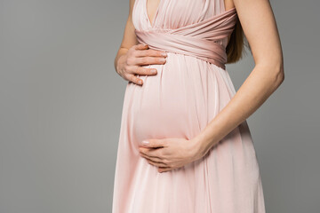 Cropped view of fashionable and long haired woman in pink dress touching belly while standing...