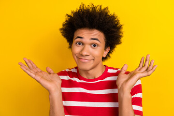 Photo of unsure uncertain man wear striped t-shirt rising arms shrugging shoulders isolated yellow color background