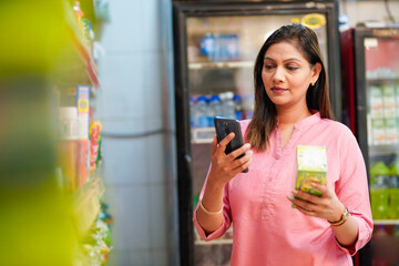 Indian woman checking product information in smartphone at supermarket