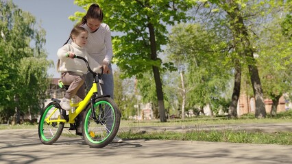 little daughter learns ride two-wheeled bicycle for first time, mother daughter, smile teeth laughing child bike plays park, time together, happy cute girl learns ride bike while driving, mother