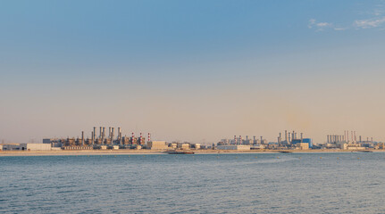 Fototapeta premium Air pollution from power plant chimneys. view from Bluewater island in Dubai city. Urban landscape smoked polluted atmosphere from emissions of plants and factories, view of pipes with color smoke
