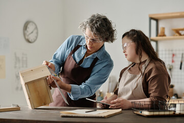 Girl with down syndrome and carpenter using ruler to measure house together while working in...