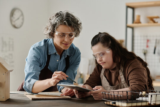 Girl with down syndrome using digital tablet and discussing future project with carpenter in workshop