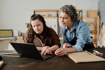 Carpenter using laptop with her student and discussing online project together with girl during...