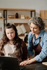 Vertical image of carpenter using laptop in her work in workshop together with girl with down...