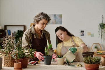 Girl with down syndrome watering plants while planting them together with florist in the room