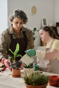 Vertical image of girl with down syndrome caring about plants together with florist