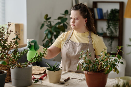 Girl with down syndrome using sprayer to spray green plants in pots