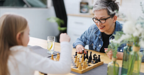 Joy my, grandmother plays chess with her granddaughter at the table.