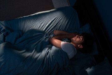 Top view of young man sleeping on cozy bed in his bedroom at night. Blue nightly colors with light...