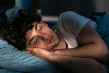Handsome young man sleeping on pillow in dark room at night, resting at night time. Healthy sleep