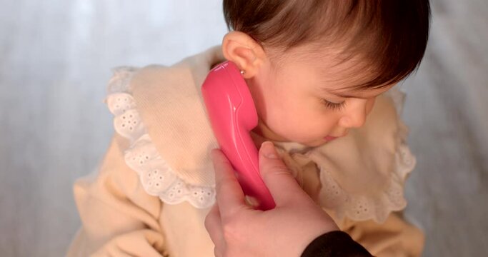 Portrait of a child toddler telephone receiver ear toy. Interaction and play with objects. The development of the child, the girl shows interest.