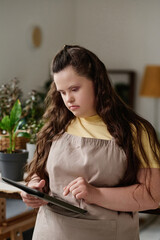 Vertical image of florist in uniform concentrating on her online work on tablet pc