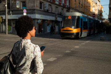 African woman walking alone, being a tourist, holding her phone, train passing in the background.
