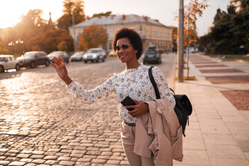 African female tourist waving at the taxi ride, being at the downtown.