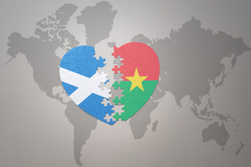 puzzle heart with the national flag of burkina faso and scotland on a world map background.Concept.
