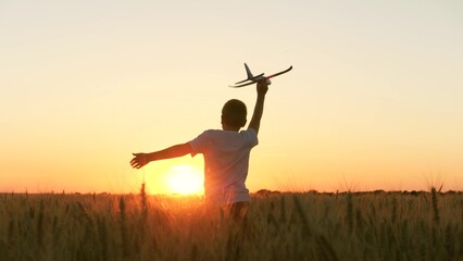 boy teenager child kid runs through field with wheat with toy plane his hands sunset, happy dream...