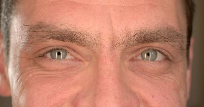 Motivation with positive mood. Close-up of men's eyes blinking, looking intently into the camera. Visual contact, blin. Narrow pupil of the eye.