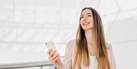 Business woman stands indoors in an office building holding a mobile phone and smiling