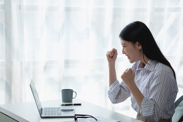 Portrait of a beautiful smiling Asian businesswoman suited to the computer desk. Small business SME online freelancer startup marketing doing business success gesture.