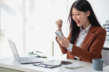 Portrait of a beautiful smiling Asian businesswoman suited to the computer desk. Small business SME online freelancer startup marketing doing business success gesture.