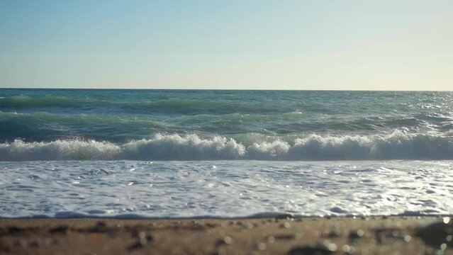 Waves of Mediterranean sea crashing on sandy beach on Cyprus in slow motion. Wide shot picturesque seascape in sunshine outdoors