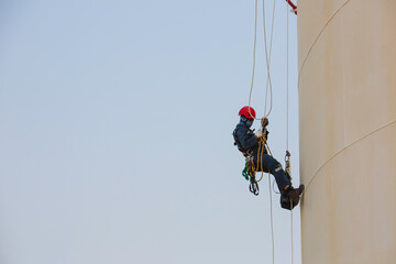 Male worker rope access industrial working at height tank oil wearing harness, helmet safety equipment rope access inspection of thickness tank