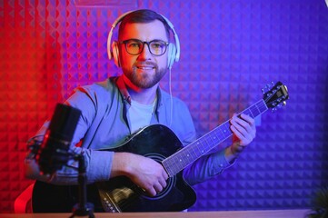 Close up man in headphones playing guitar and singing, recording on smartphone, musician artist recording new song video for social network, blogger or music teacher shooting course in home studio