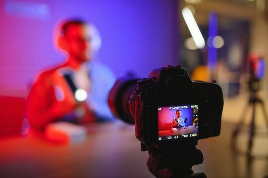 Male technology blogger recording video blog or vlog review of new smartphone, showing it on camera at home studio. Blogging, Work from Home concept. Selective focus. Web Banner