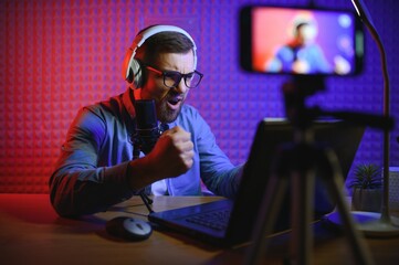 Plakat streamer is streaming online content,metaverse ar vr,gaming and esports concept.Happy man gamer wear headphone competition video game online with Laptop computer in colorful neon lights.