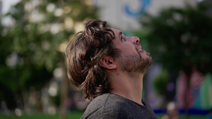 One young man gazing up at sky with HOPE. A male caucasian person in 30s turning head upwards observing sunny day