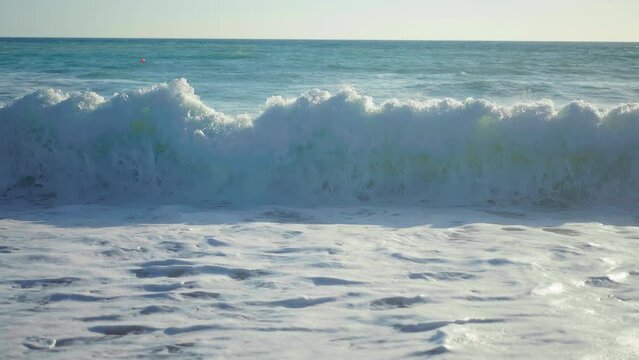 Front view Mediterranean sea waves crashing on golden sand with white foam in slow motion. Crystal clear ocean water rolling on coast in sunshine on Cyprus