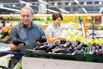 elderly man chooses eggplants in vegetable and fruit department