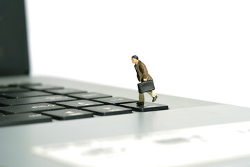 Miniature tiny people toy figure photography. A businessman running above keyboard notebook laptop carrying briefcase. Isolated on white background