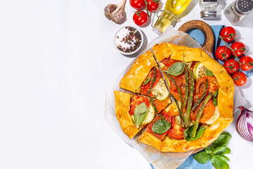 Fresh baked homemade vegetable vegan pie, Crunchy savoury galette tart  with olives, zucchini, tomatoes, asparagus, with ingredients for cooking, spices, olive oil